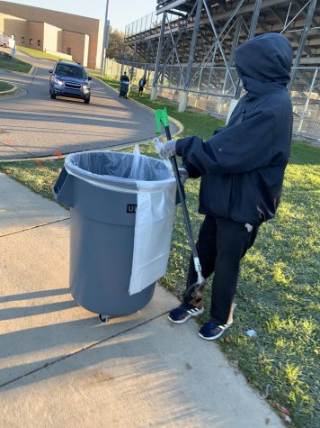 Student picks up trash by the riverbank stadium at Huron High School. 