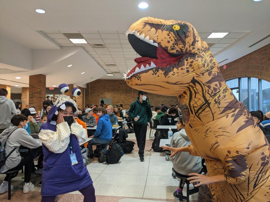 Veronic Choe in a dinosaur costume for Halloween posing with a student. 