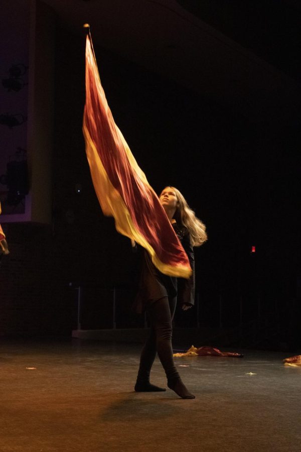 Raising her flag high into the air, sophomore Kendra Muenz performs a color guard routine to Golden Hour, by JVKE.