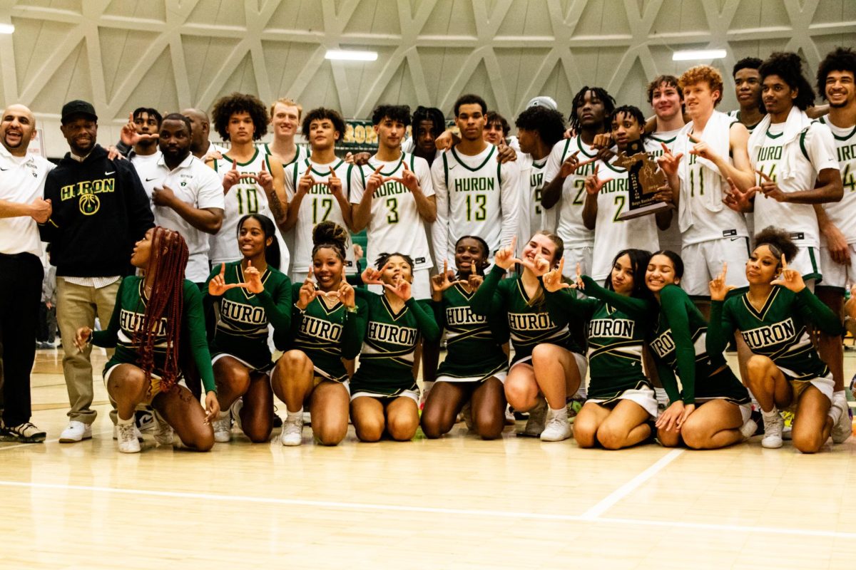 Hurons men’s varsity basketball team, varsity cheer team, and principal Ché Carter posing for a picture at center court after winning the district championship.