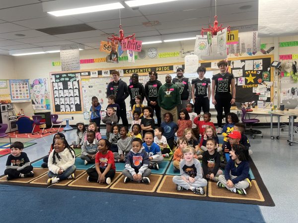 Varsity Football players Bryan White, Kyce Shamma, Michael Woods, LaMar Ashford, Diego Ramero, Aaron Weiner, and Coach Jamonte Love take a group photo with the kindergarten class after they’re done reading. Photo courtesy of Coach Love.