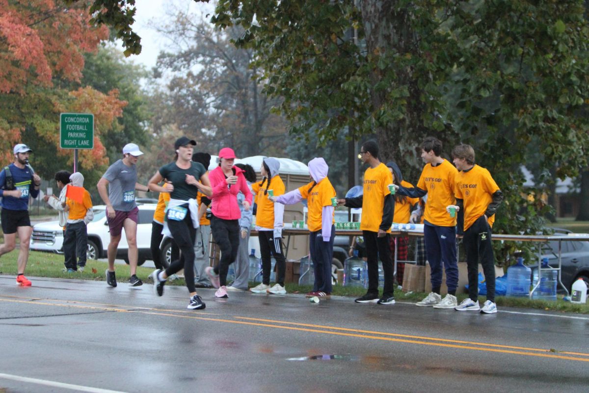 Huron NHS students stand in a line prepared to pass water and Gatorade to the athletes running by. 