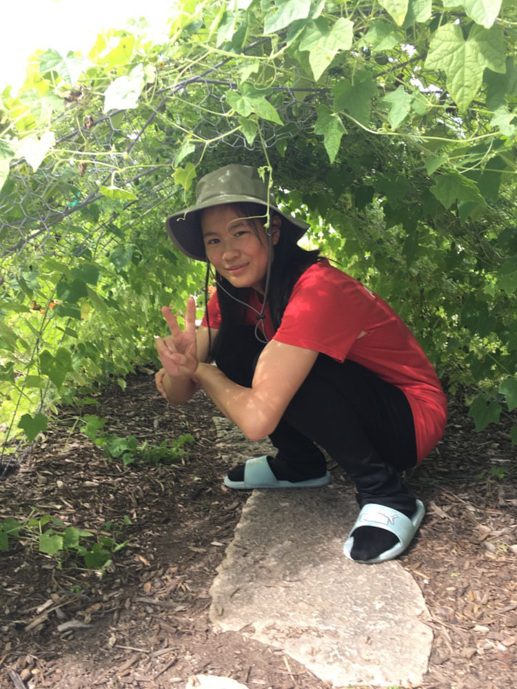 Janet Yang kneeling underneath a bush. Courtesy of Yang. 