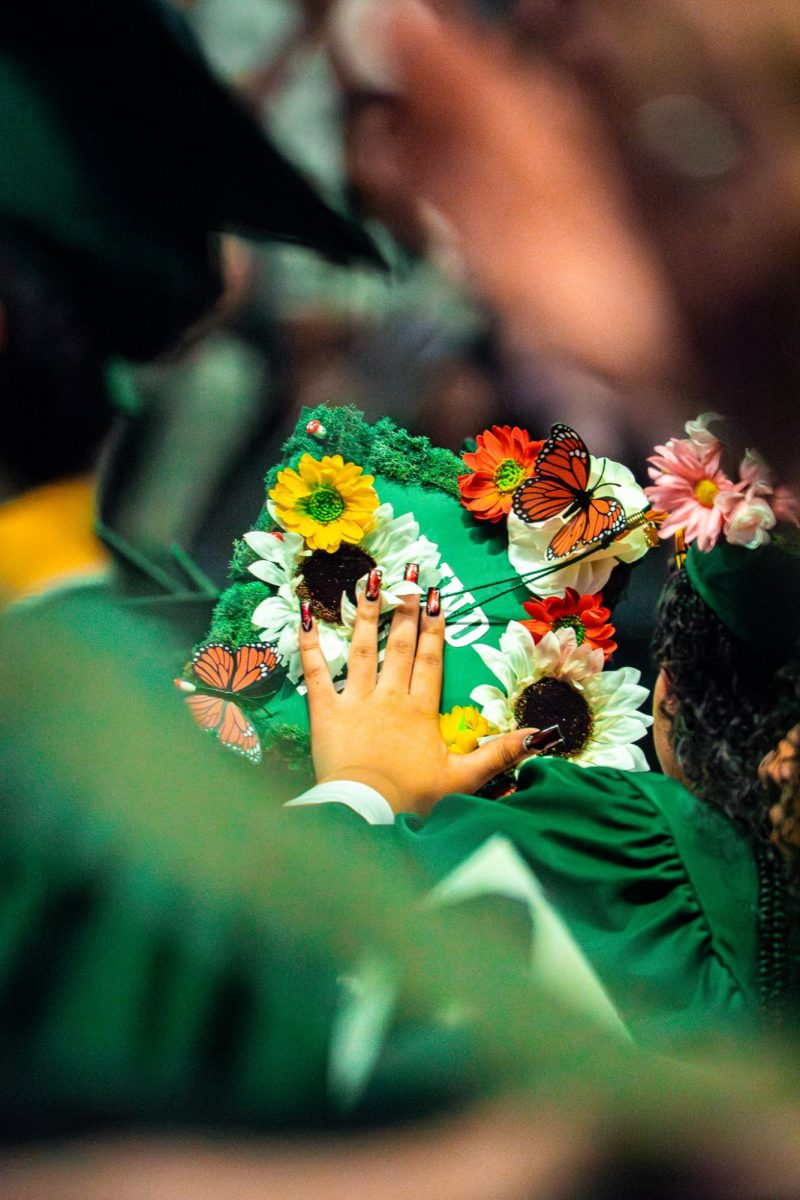 Students support one another by helping keep each other's caps on while getting up to walk on stage.
