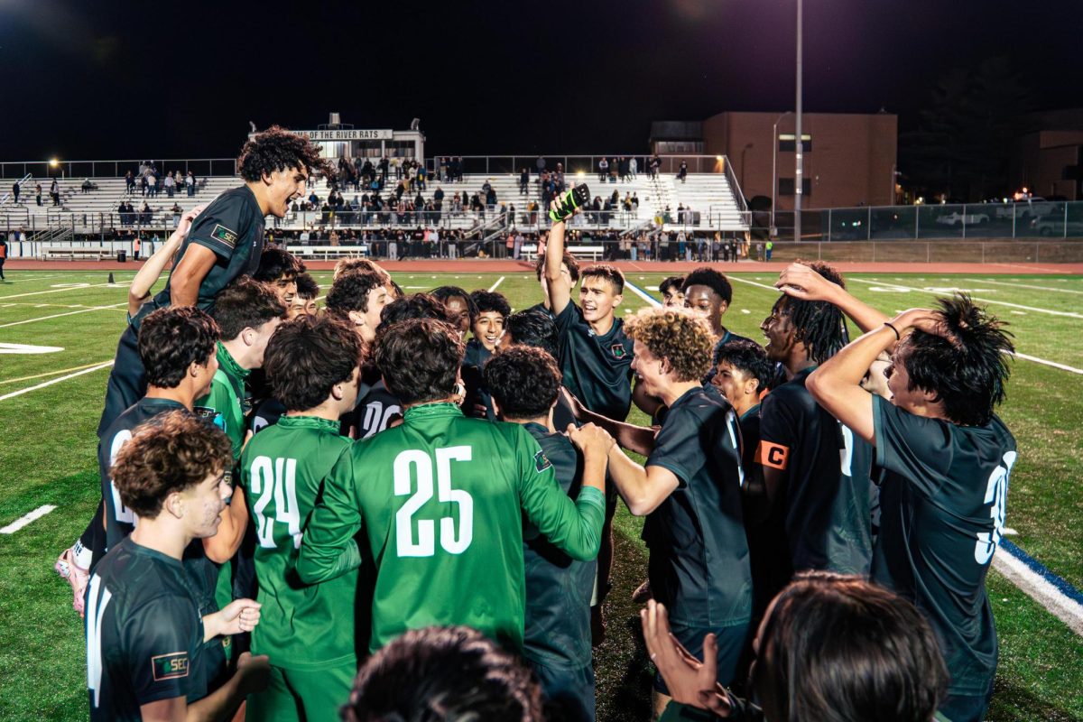 The Huron Men's Varsity Soccer Team celebrate around Coach Luis Gomez-Dominguez. 