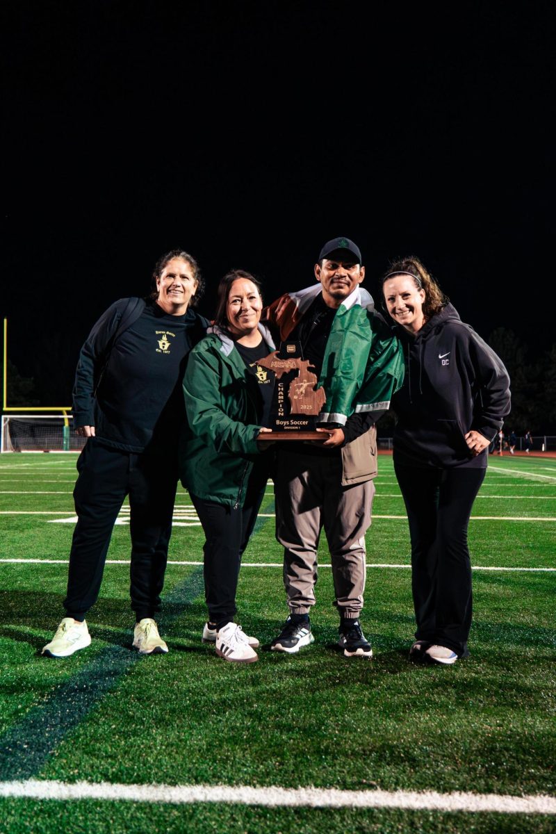 Coaches Suzanne Dickie, Angela Heflin, Luis Gomez-Dominguez, and Sara Badalamente (left to right) pose for a picture with the trophy after the game. 