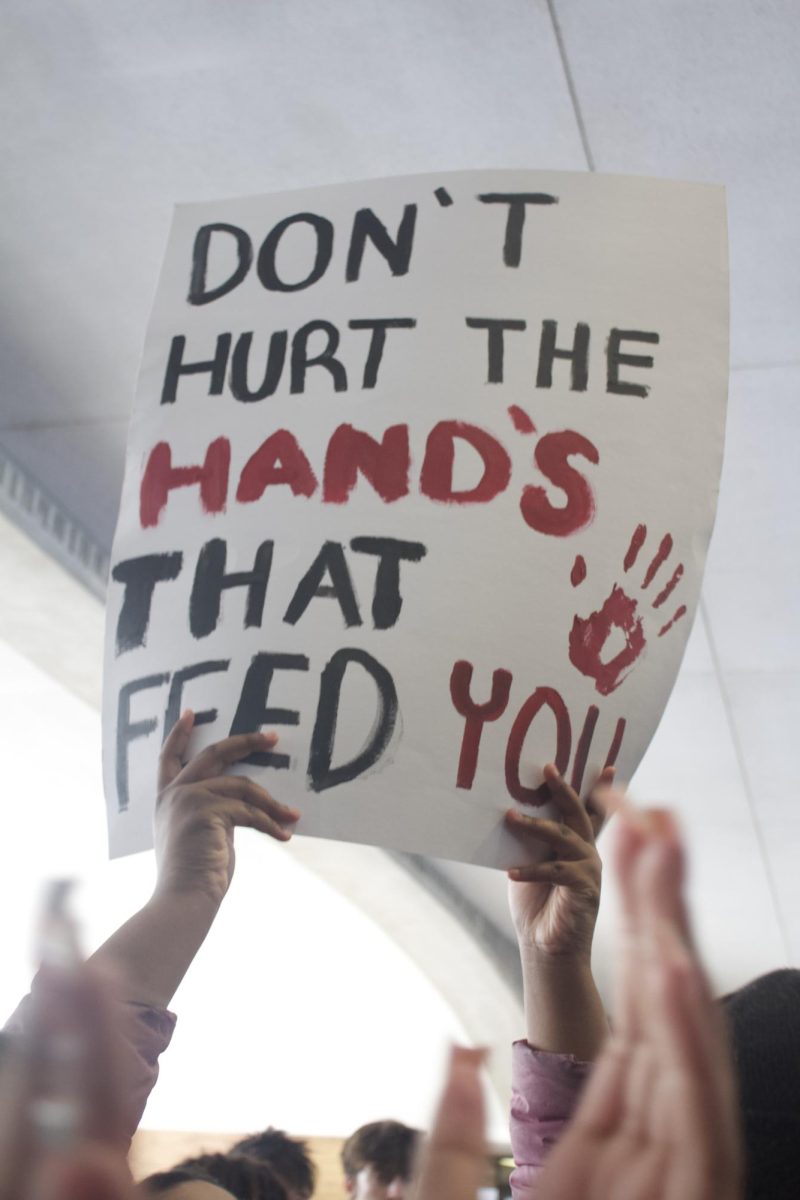A Huron student holds a poster that reads, "Don't hurt the hands that feed you." 
