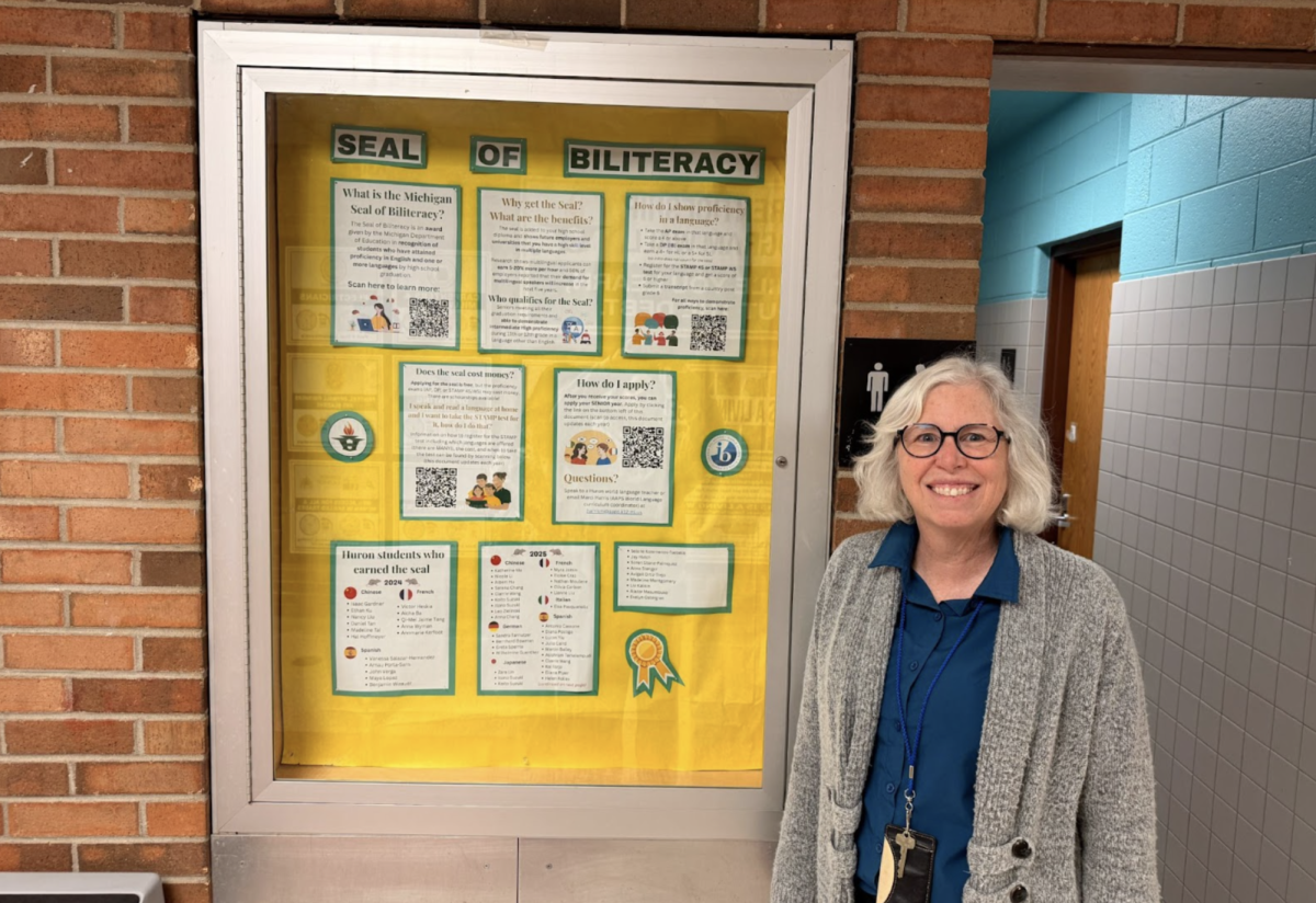 French teacher and co-World Language Department Chair Mary Clair Wissman posing next to the Seal of Biliteracy bulletin.