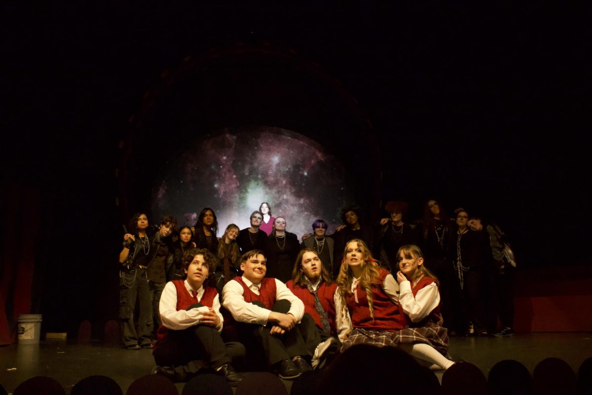 Huron freshman Roya McAllister (Ricky) sits with Community senior David Constantin (Noel), Huron seniors Fynn Murphy (Mischa) and Téa Nelson (Constance), and Huron sophomore Amelie Sasena (Ocean) as the ensemble gathers behind them.